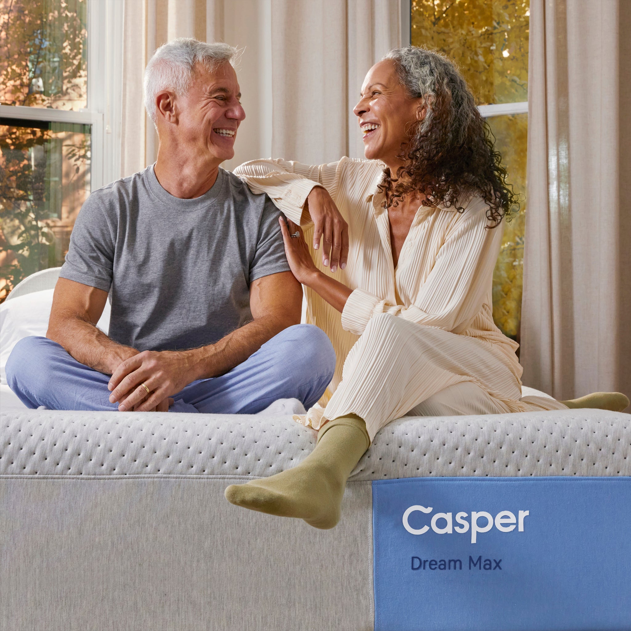 Couple sitting on Dream Max Mattress by Casper | Maximum support with hybrid foam and coils